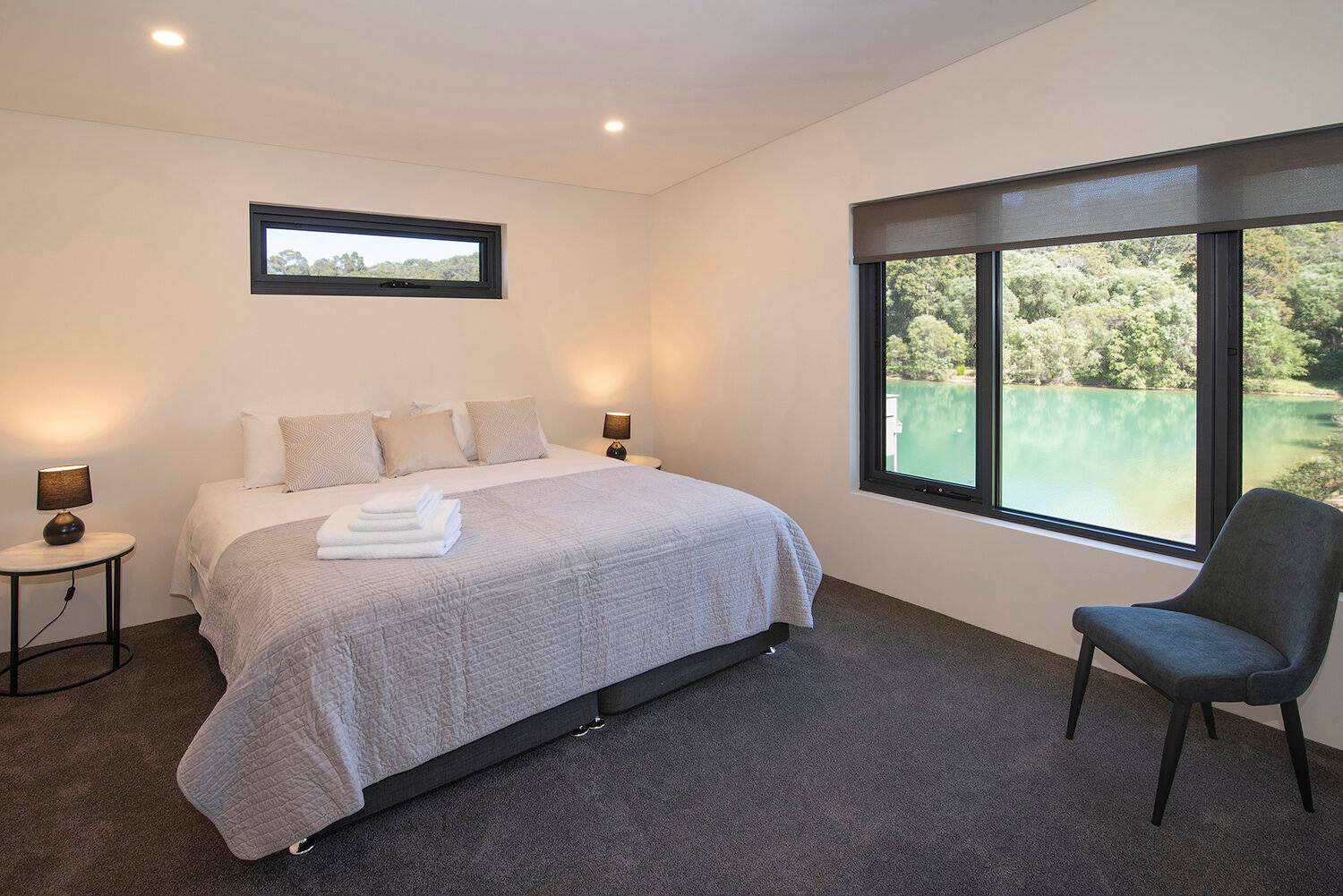Mercury Light Filtering Roller Blind opt Spacious bedroom with lake view and soft lighting.